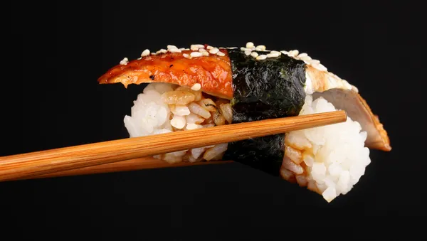 Tenendo sushi con bacchette isolate su nero — Foto Stock