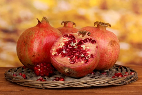 Ripe pomegranates on wicker cradle on wooden table on autum background — Stock Photo, Image