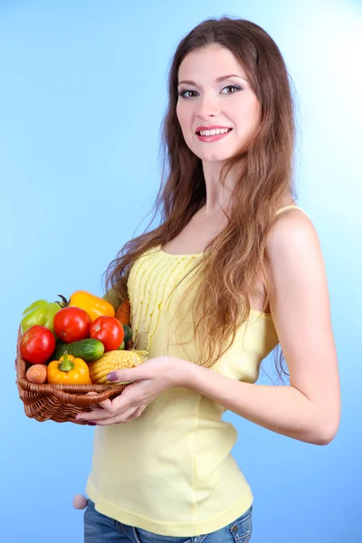 Mulher bonita com legumes em cesta de vime no fundo azul — Fotografia de Stock