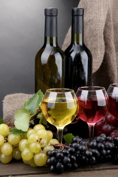 Garrafas e copos de vinho e uvas sobre fundo cinzento — Fotografia de Stock