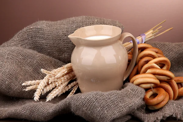Pot van melk, smakelijke bagels en spikelets op houten tafel, op bruin pagina — Stockfoto