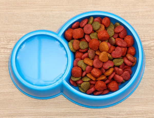 dry dog food and water in blue bowl on wooden background