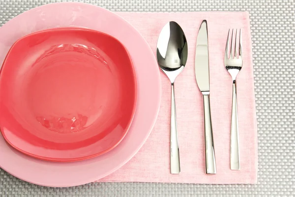 Platos vacíos rosados con tenedor, cuchara y cuchillo sobre un mantel gris —  Fotos de Stock