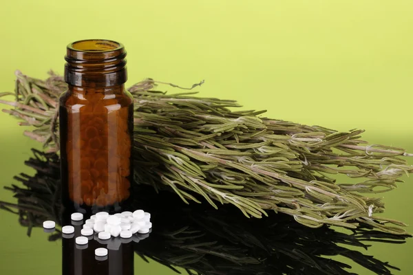 Garrafa com comprimidos e ervas em fundo verde. conceito de homeopatia — Fotografia de Stock