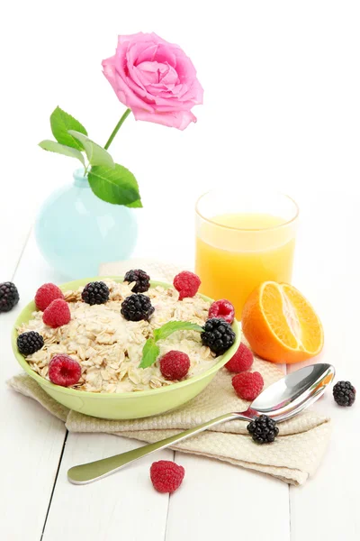 Вкусная овсянка с ягодами и стаканом сока, на белом деревянном столе — стоковое фото