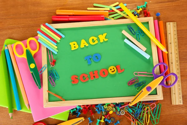 Small chalkboard with school supplies on wooden background. Back to School — Stock Photo, Image
