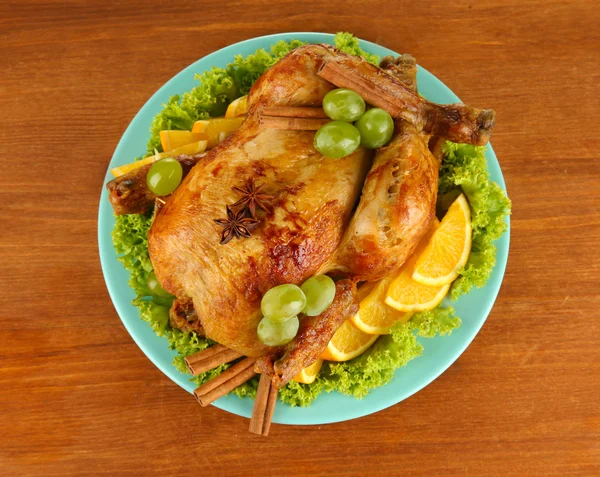 Целая жареная курица с салатом, виноградом, апельсинами и специями на синей тарелке на деревянном фоне крупным планом — стоковое фото