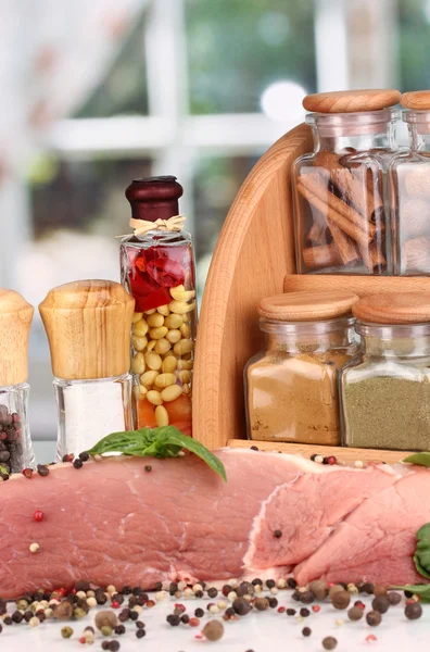 Un gros morceau de porc mariné avec des herbes et des épices sur une table blanche sur fond de fenêtre — Photo