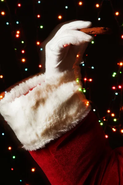 Papai Noel mão segurando biscoito de chocolate no fundo brilhante — Fotografia de Stock