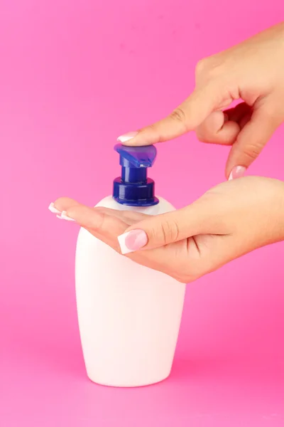 Vrouw knijpen lotion op haar hand, op roze achtergrond close-up — Stockfoto