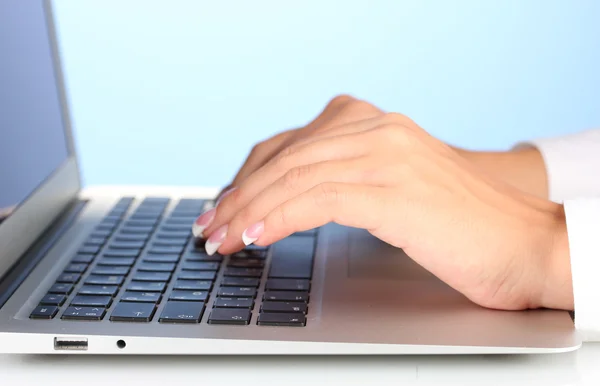 笔记本电脑键盘上打字的手在蓝色背景上关闭 — 图库照片