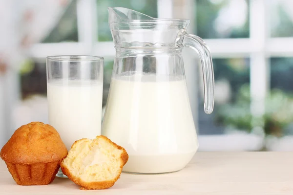 Sürahi ve bardak süt ile kekler penceresi arka plan üzerinde ahşap masa üzerinde — Stok fotoğraf