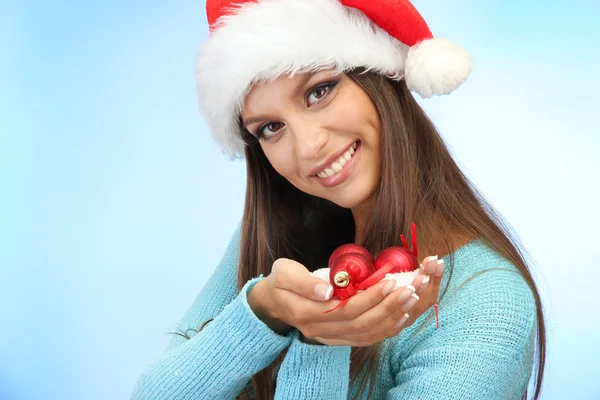 Schöne junge Frau hält Schnee mit Weihnachtskugeln, auf blauem Hintergrund — Stockfoto