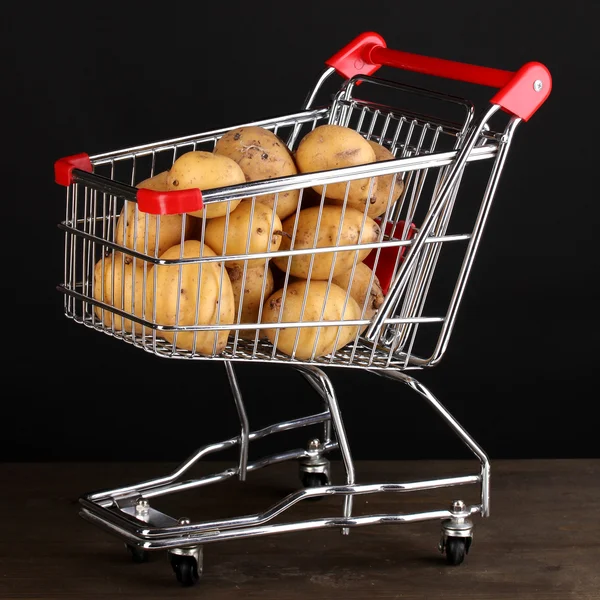 Ripe potatoes in trolley on wooden table on black background — Stock Photo, Image