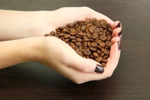 Vrouwelijke handen met koffiebonen, op houten achtergrond — Stockfoto