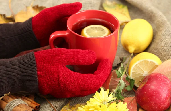 Manos sosteniendo taza de bebida caliente y hojas de otoño, sobre fondo de arpillera —  Fotos de Stock