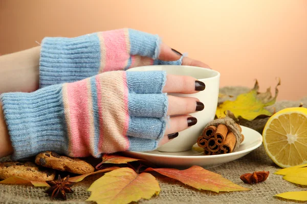 Mani in possesso di tazza di bevanda calda e foglie autunnali, su sfondo iuta — Foto Stock