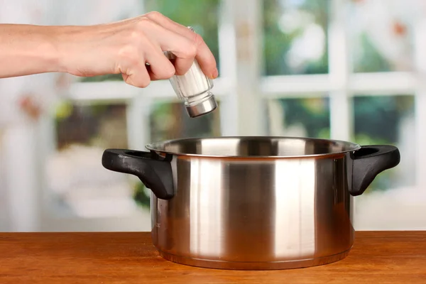 Hand adding salt using salt shaker on bright background — Stock Photo, Image