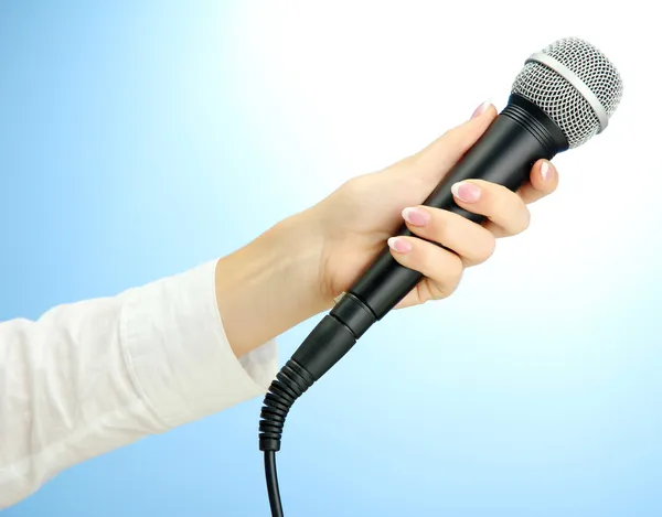 Main féminine avec microphone, sur fond bleu — Photo