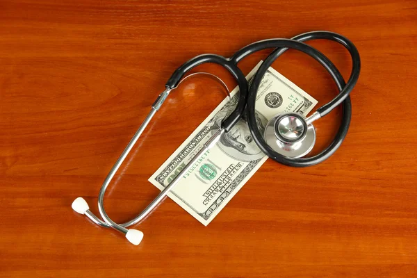 Healthcare cost concept: stethoscope and dollars on wooden background — Stock Photo, Image