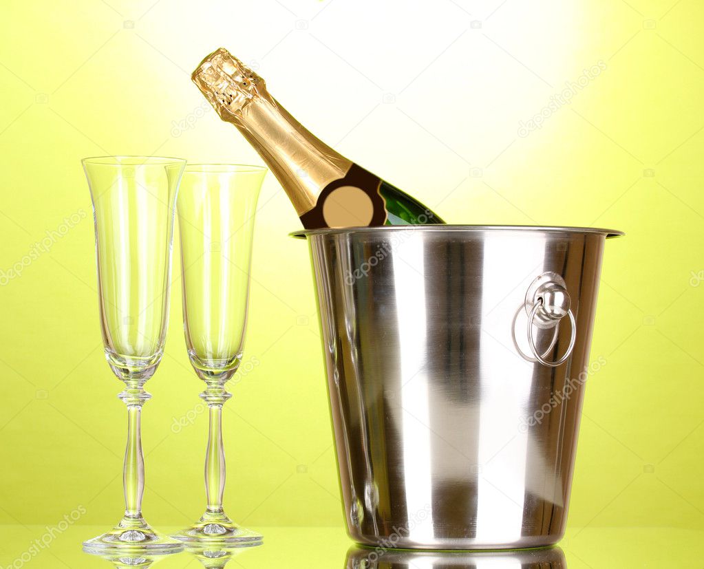 Champagne bottle in bucket with ice and glasses on green background