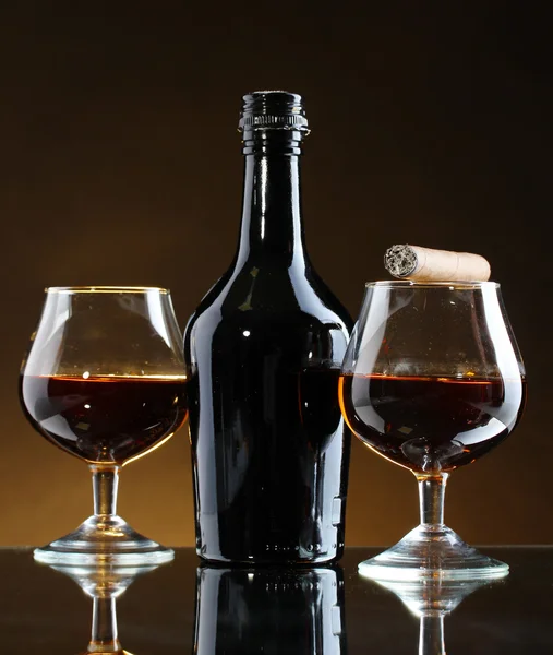 Botella y vasos de brandy y cigarro sobre fondo marrón — Foto de Stock