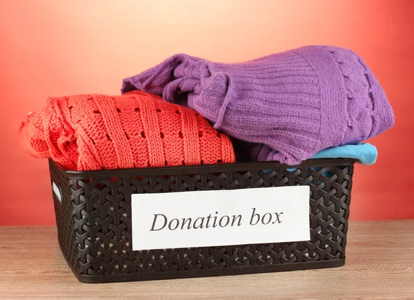 Caja de donación con ropa sobre fondo rojo —  Fotos de Stock