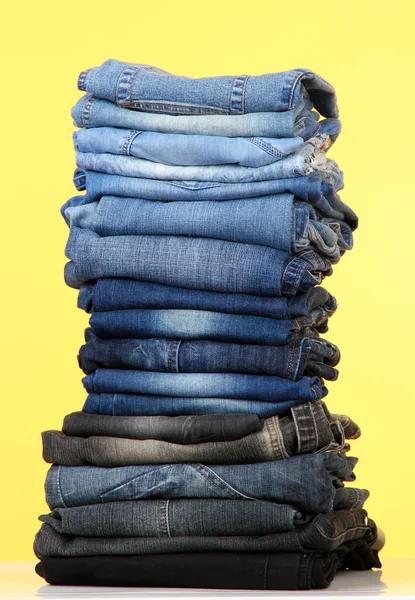 Many jeans stacked in a pile on yellow background — Stock Photo, Image