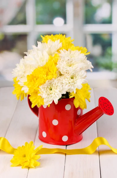 Red watering can of peas with flowers on white wooden table on window background — Stock Photo, Image