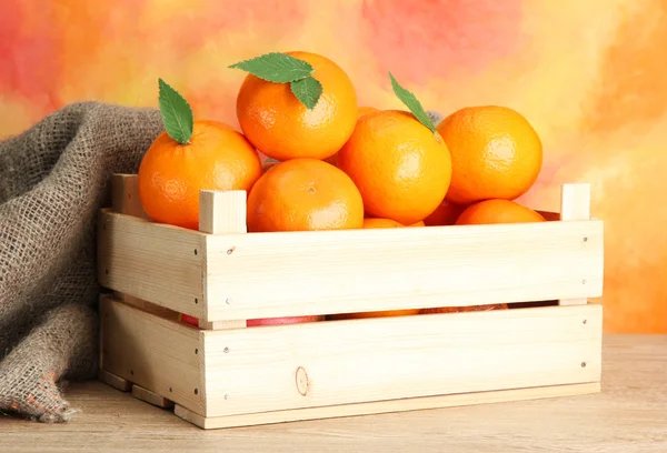 Mogen läckra tangeriner med blad i trälåda på bordet på orange bakgrund — Stockfoto