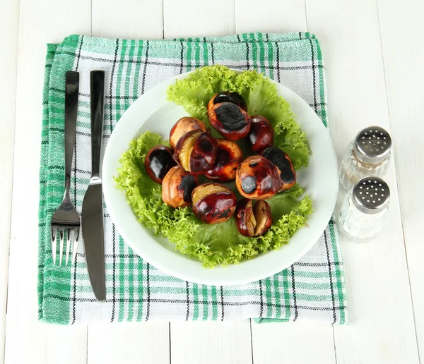 Castañas asadas con lechuga en el plato sobre fondo de madera blanca —  Fotos de Stock