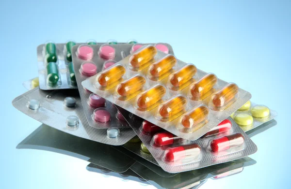 Kapsułki i tabletki pakowane w blistry, na niebieskim tle — Zdjęcie stockowe