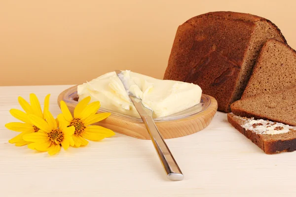 Butter on wooden holder and bread on wooden table on beige background — Stock Photo, Image