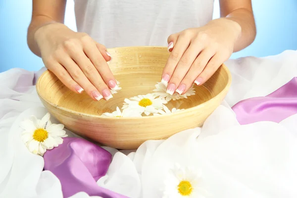 Manos de mujer con cuenco de madera de agua con flores, sobre fondo azul —  Fotos de Stock