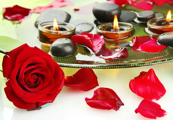Курортные камни с лепестками роз и свечами в воде на тарелке — стоковое фото