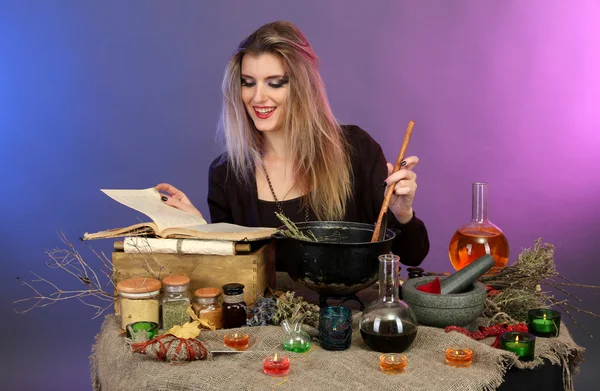 Halloween-Hexe rührt in Giftsuppe in ihrem Hexenkessel auf farbigem Hintergrund — Stockfoto