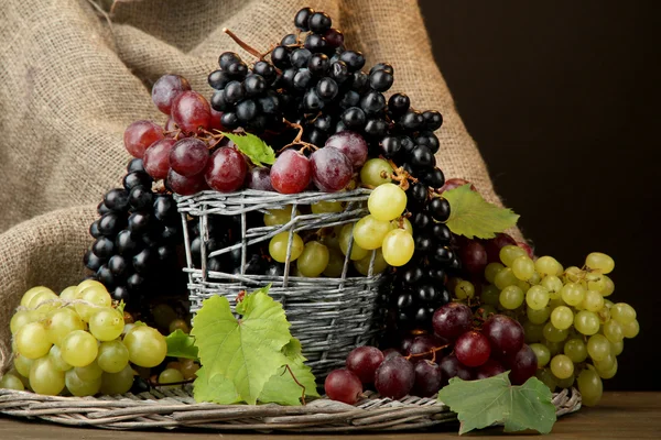 Assortment of ripe sweet grapes in basket, on brown background — Stock Photo, Image