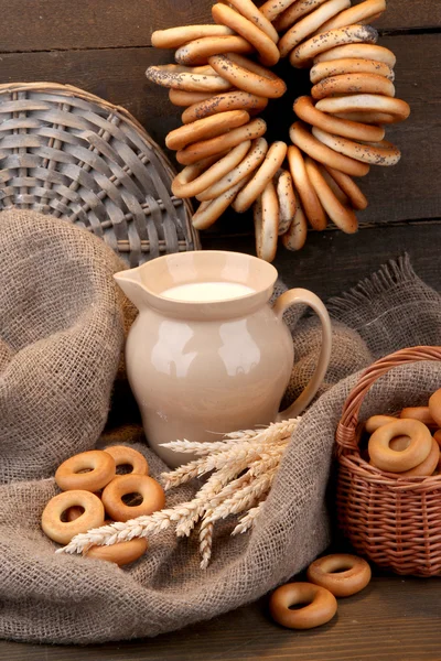 Jar of milk, tasty bagels and spikelets on wooden background — Stock Photo, Image