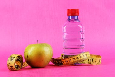 şişe su, elma ve pembe bir arka plan üzerinde ölçüm bandı