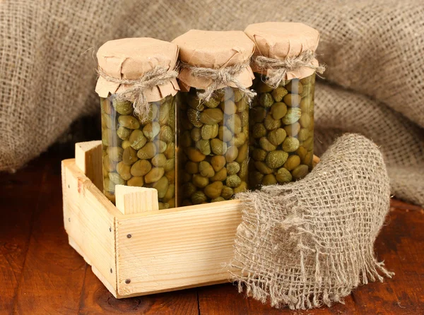 Glass jars with tinned capers on sack background close-up — Stock Photo, Image