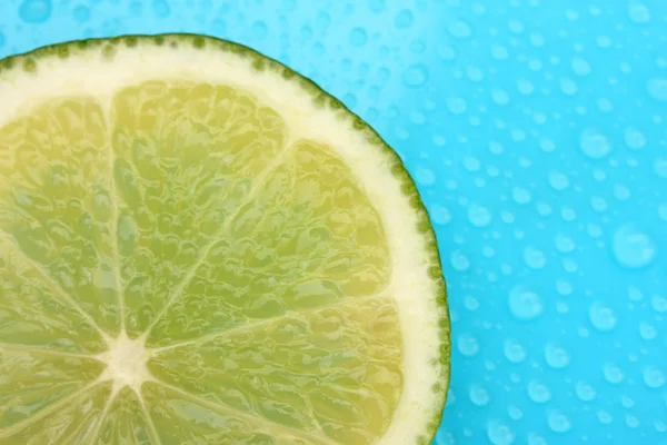 Slice of lime with drop on blue background — Stock Photo, Image