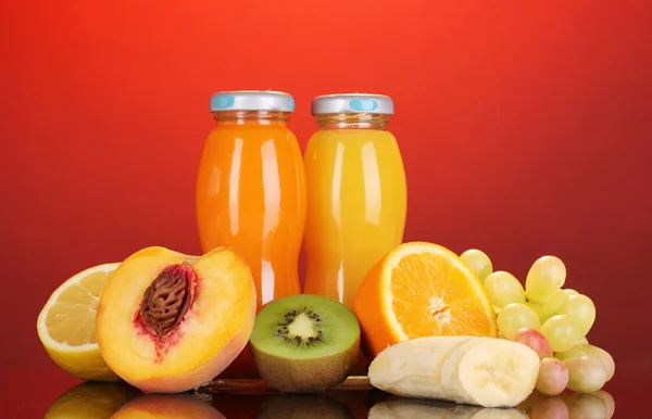 Délicieux jus de fruits multiples dans une bouteille et des fruits à côté sur fond rouge — Photo