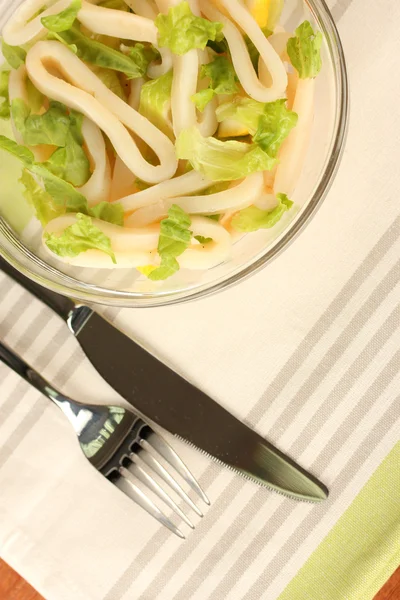 Салат из колец кальмара, лимона и салата в стеклянной чаше на полосатой скатерти крупным планом — стоковое фото