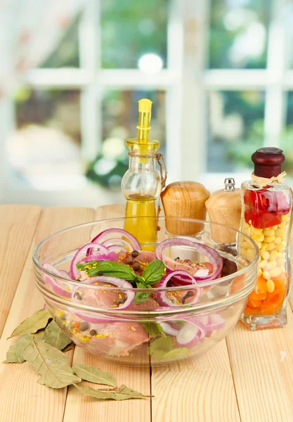 Een groot stuk van varkensvlees gemarineerd in kom met kruiden, specerijen en koken olie op houten tafel op achtergrond van venster — Stockfoto