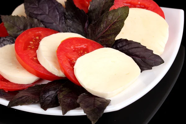 Tasty mozzarella with tomatoes on plate isolated on black — Stock Photo, Image