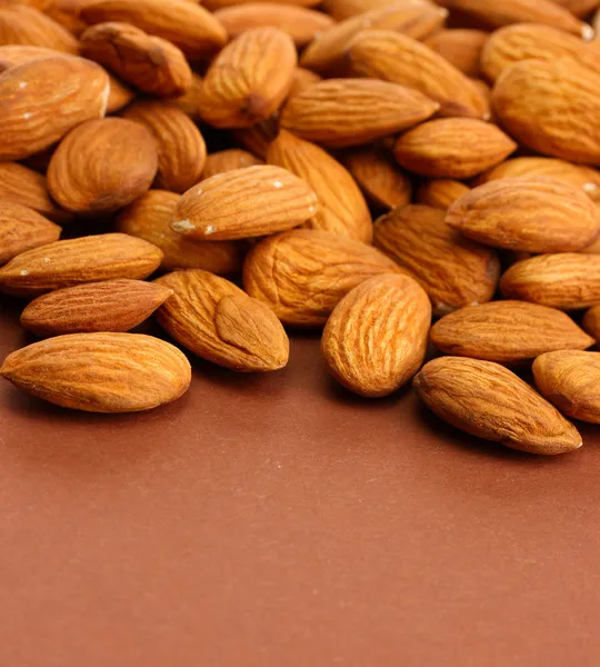 Tasty almond nuts, on brown background — Stock Photo, Image