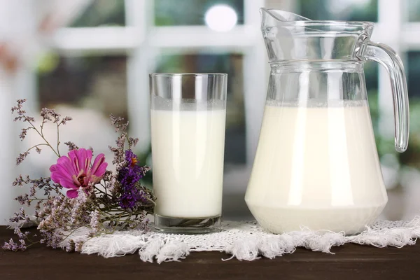 Pitcher and glass of milk on wooden table on window background