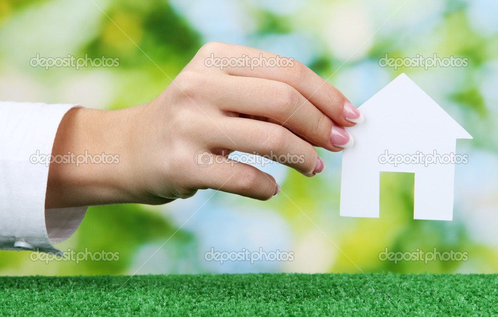 concept: woman hand with paper house on green background, close up