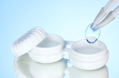 contact lenses in containers and tweezers on blue background clipart