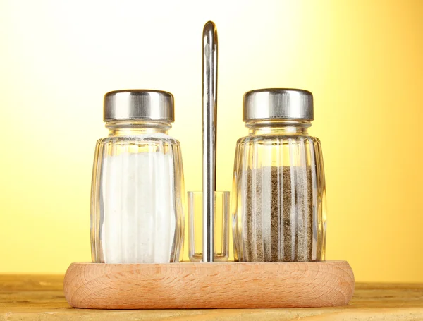Salz- und Pfeffermühlen, auf Holztisch auf gelbem Hintergrund — Stockfoto